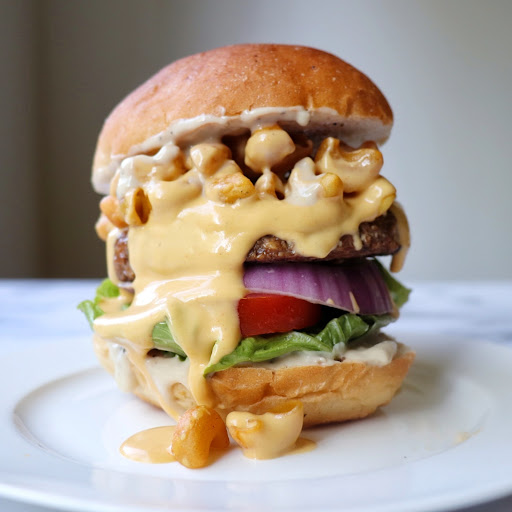 A burger overflowing with NONA cheesy, pasta-chips, and fresh toppings.