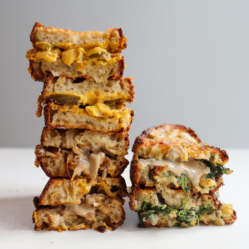 Two stacks of NONA grilled cheese. Thick slices of bread with caramelised crusts hold together gooey cheese-style sauce and fillings. 