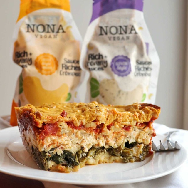 A colourful and creamy lasagna on a white plate, in front of pouches of NONA sauce.