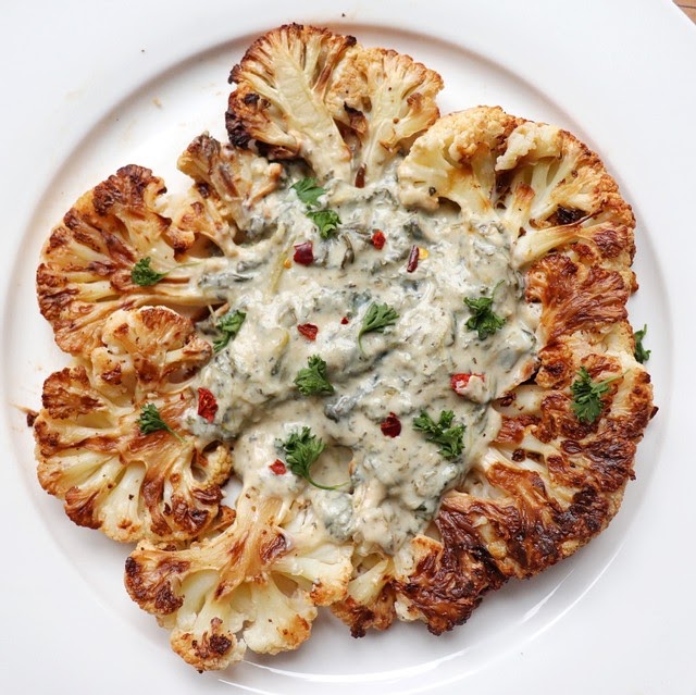 Two grilled cauliflower 'steaks' form a star, topped with tons of NONA Alfredo sauce and garnished with fresh parsley and chilli flakes.