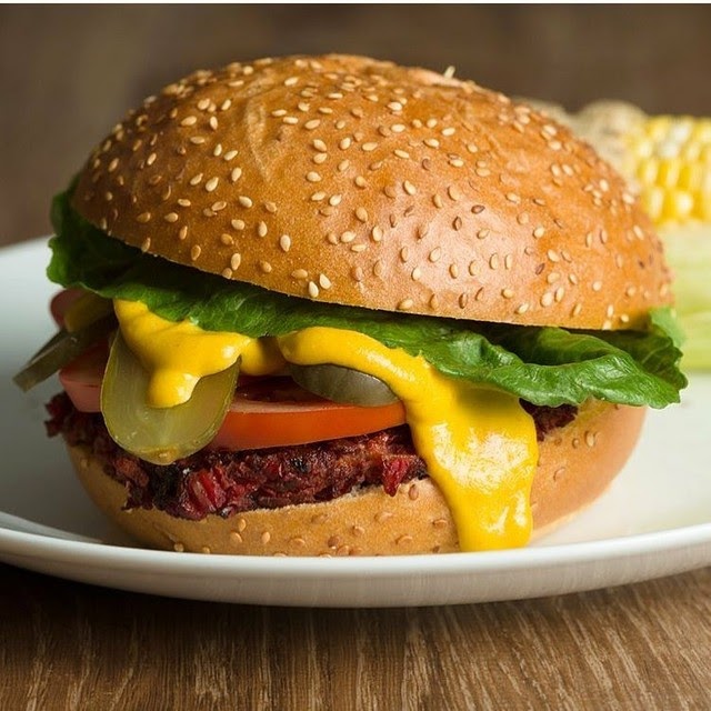 The burger in the photo has sliced tomatoes, pickles, lettuce, LOTS of NONA-Cheesy style sauce, and a sesame bun.