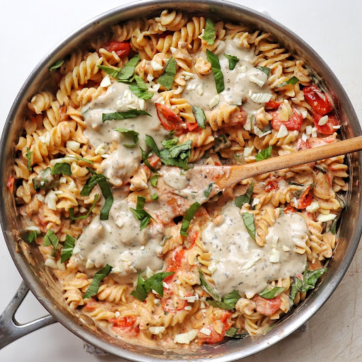 A pan filled with tomato-slathered fusilli, garnished with fresh basil and topped with heaping globs of NONA Alfredo