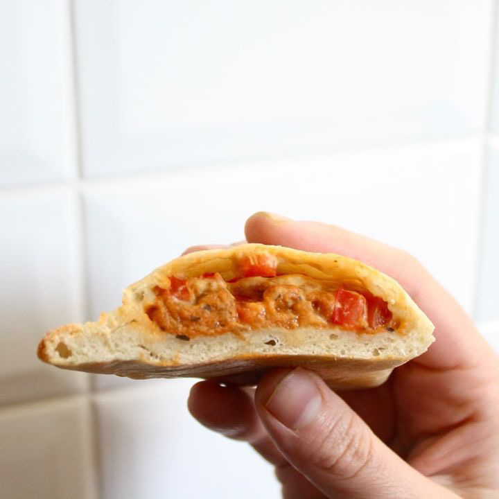 close up photo of a white hand holding a Nona Pizza pocket, cut in half showing the interior filling.